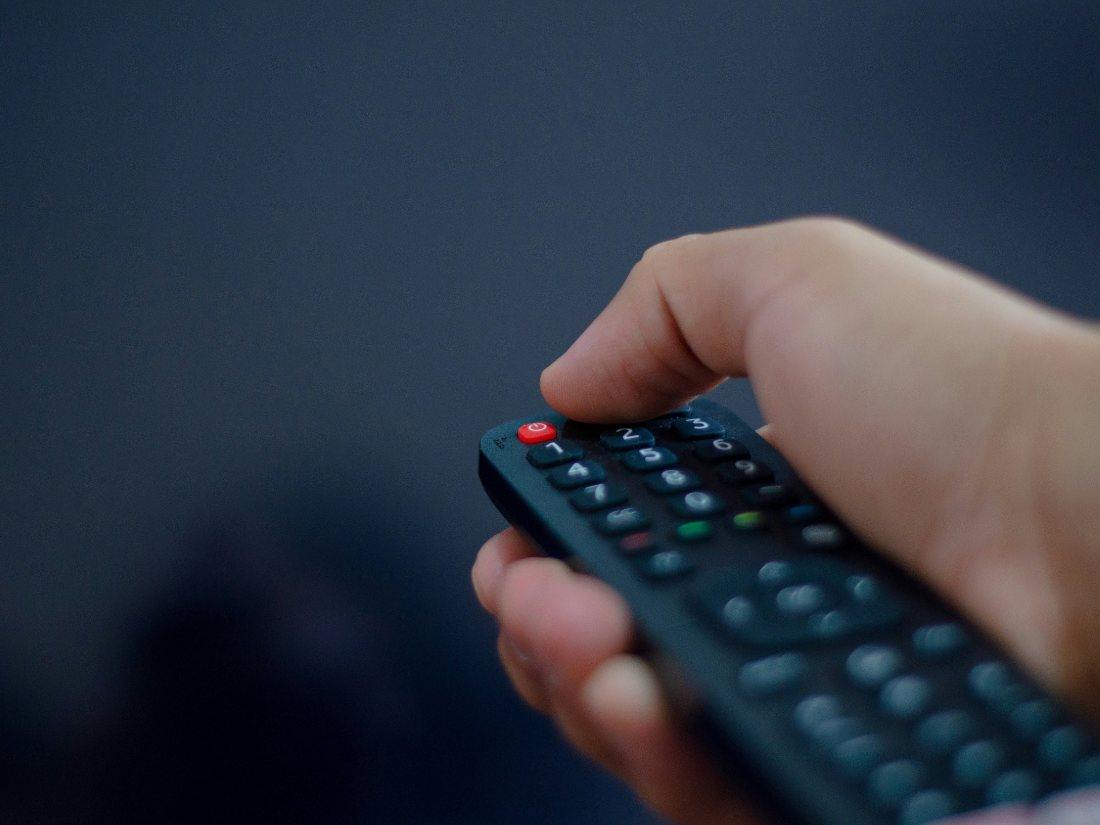 A hand holding a TV remote, ready to switch on FalconIPTV